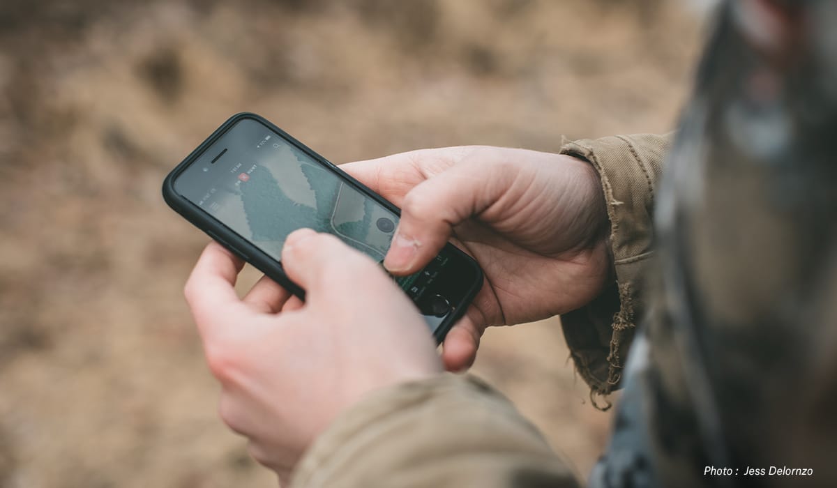 A person holds their mobile phone with the onX Hunt App on the screen.
